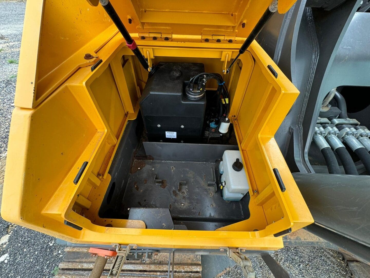 Open yellow excavator compartment with fluid reservoirs