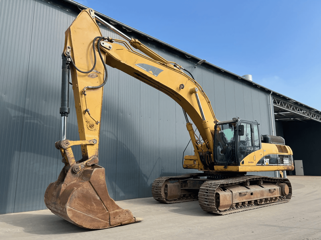 Yellow tracked excavator parked outside industrial building