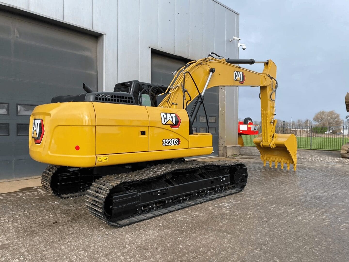Yellow Caterpillar excavator parked outside industrial building