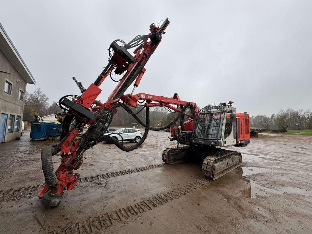 Red tracked drilling rig parked on muddy lot