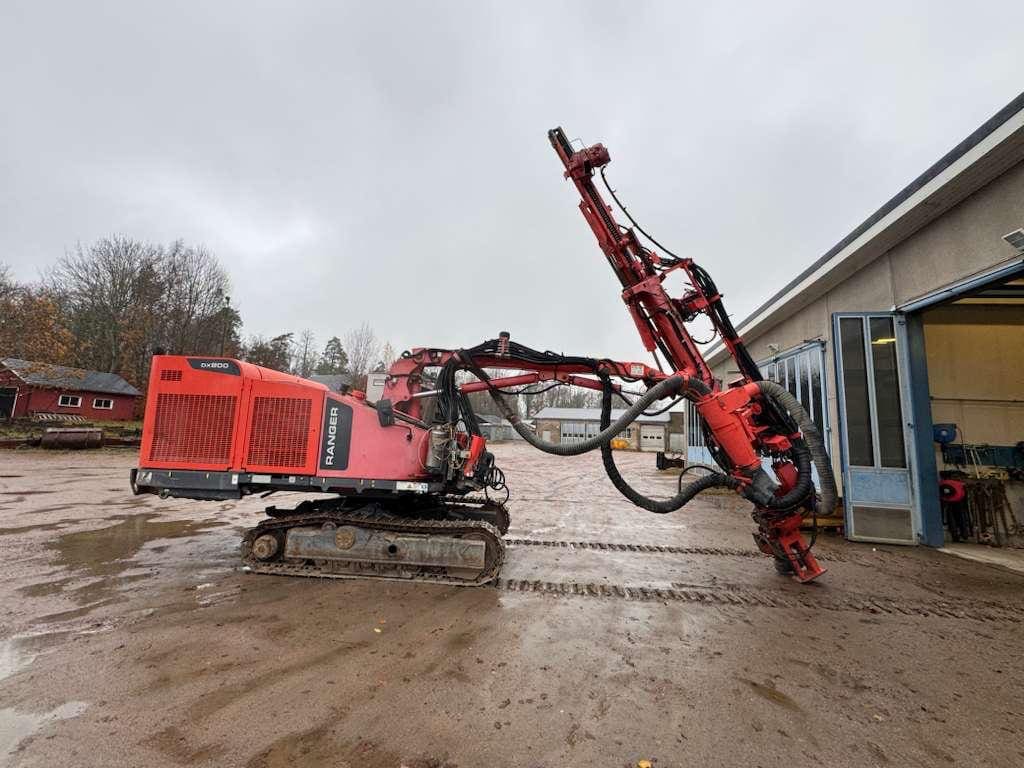Red tracked drilling rig parked beside workshop