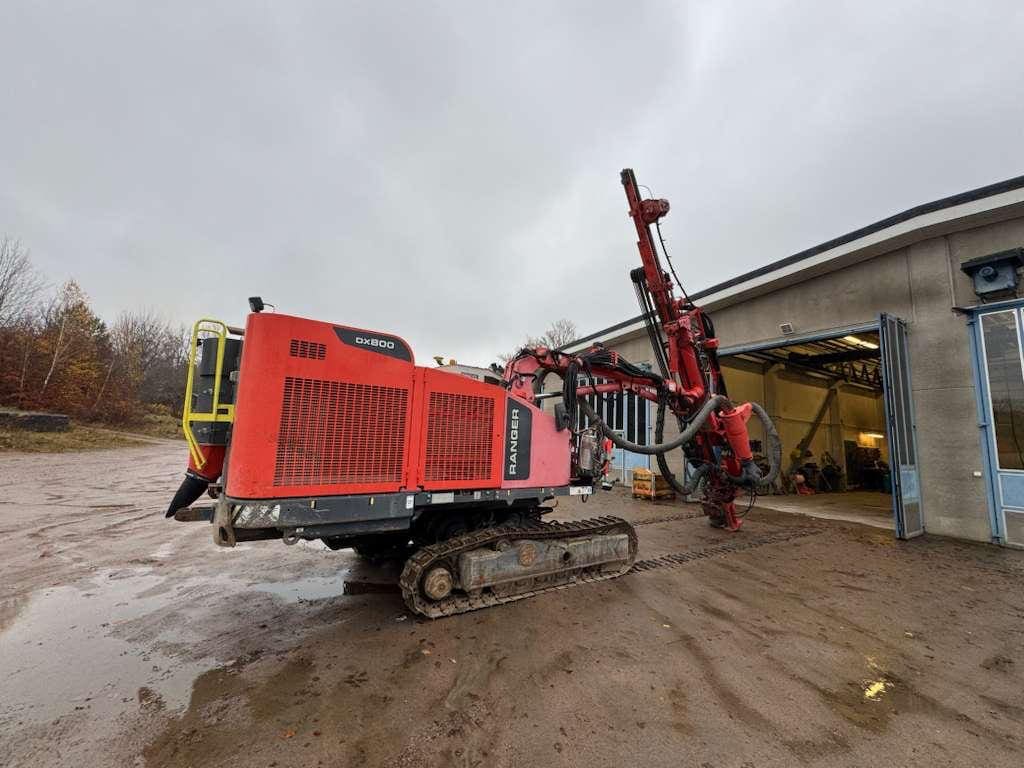 Red tracked drilling rig beside workshop