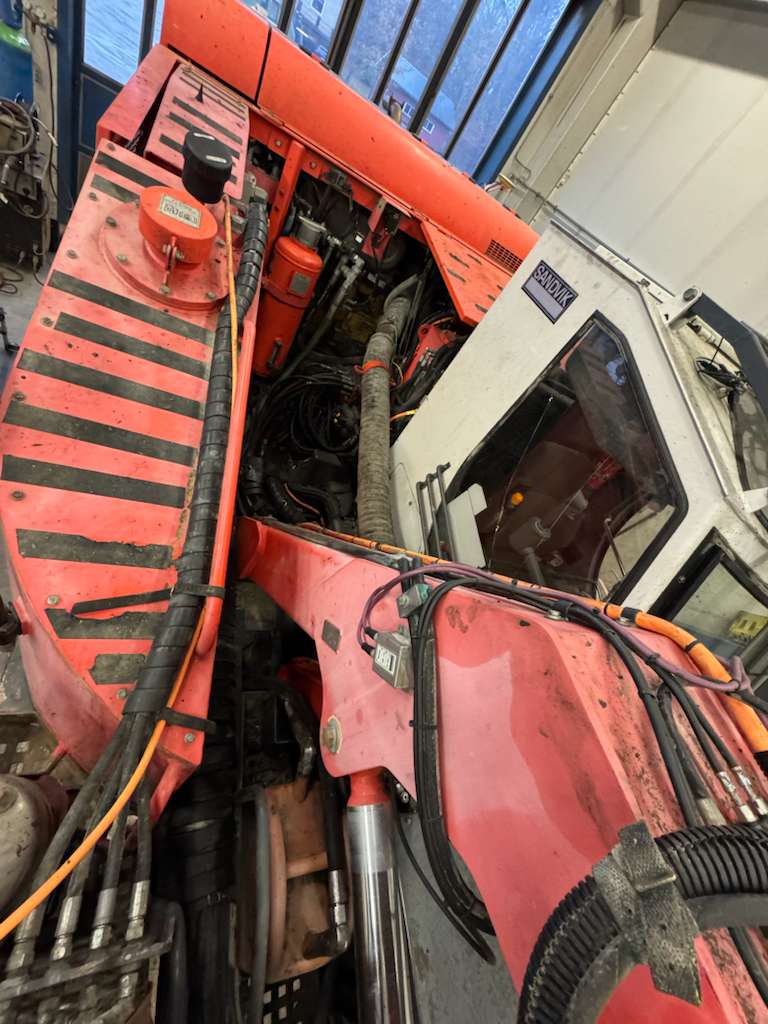 Red excavator showing exposed hydraulic hoses and cab