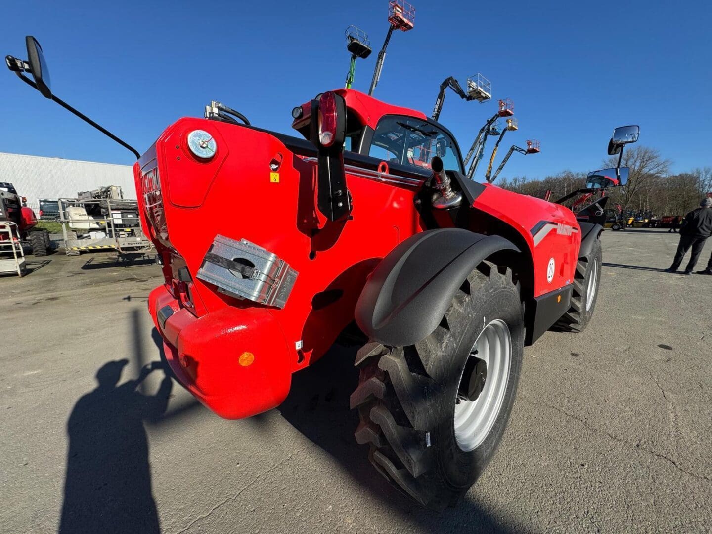 Red telehandler on asphalt under clear blue sky