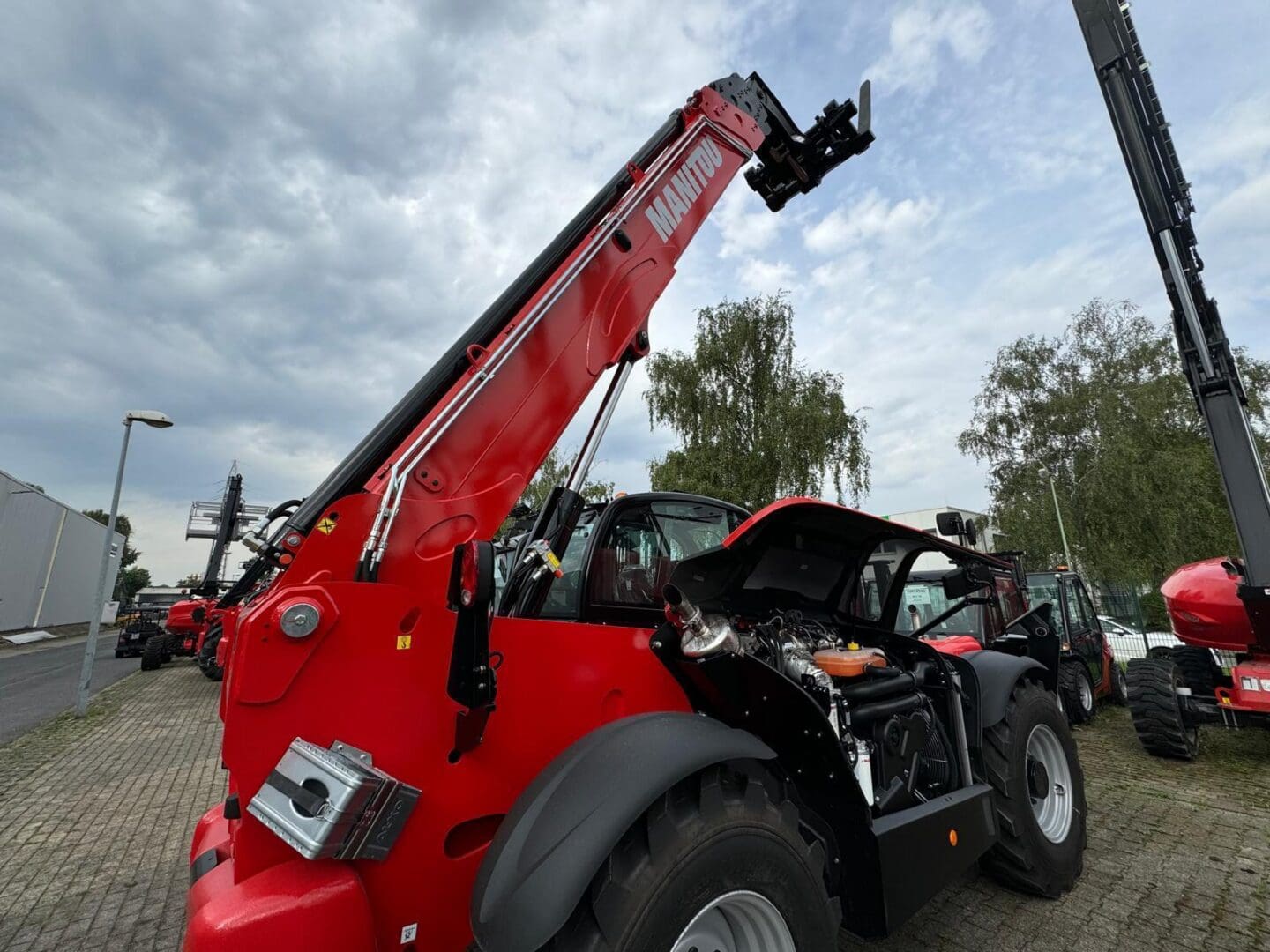 Red telehandler with raised boom, open engine