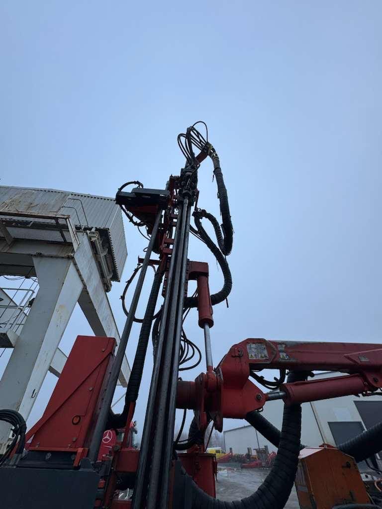 Red hydraulic drill rig under overcast sky