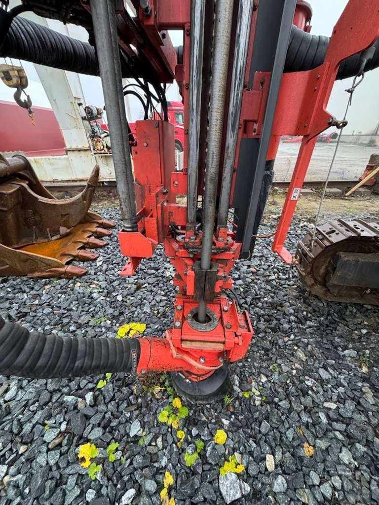 Red hydraulic drill head on gravel surface